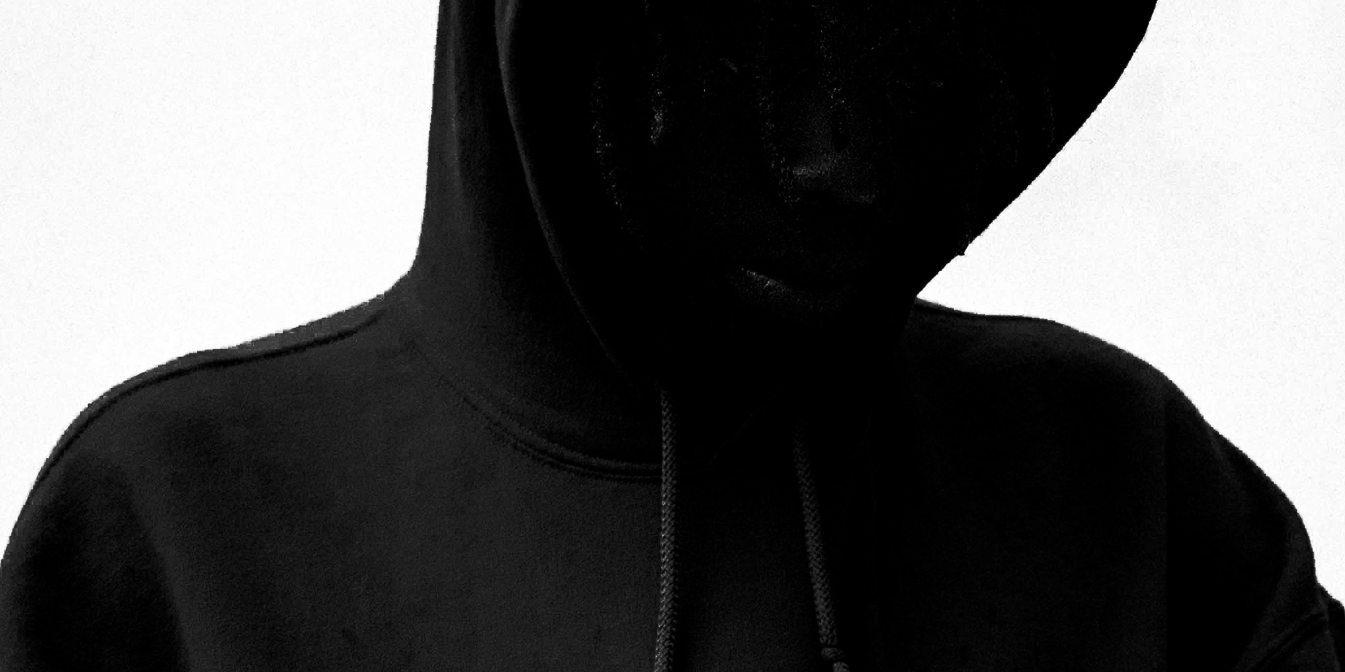 Figure in a black hooded sweatshirt, face in shadow beneath the hood, against a bright ground