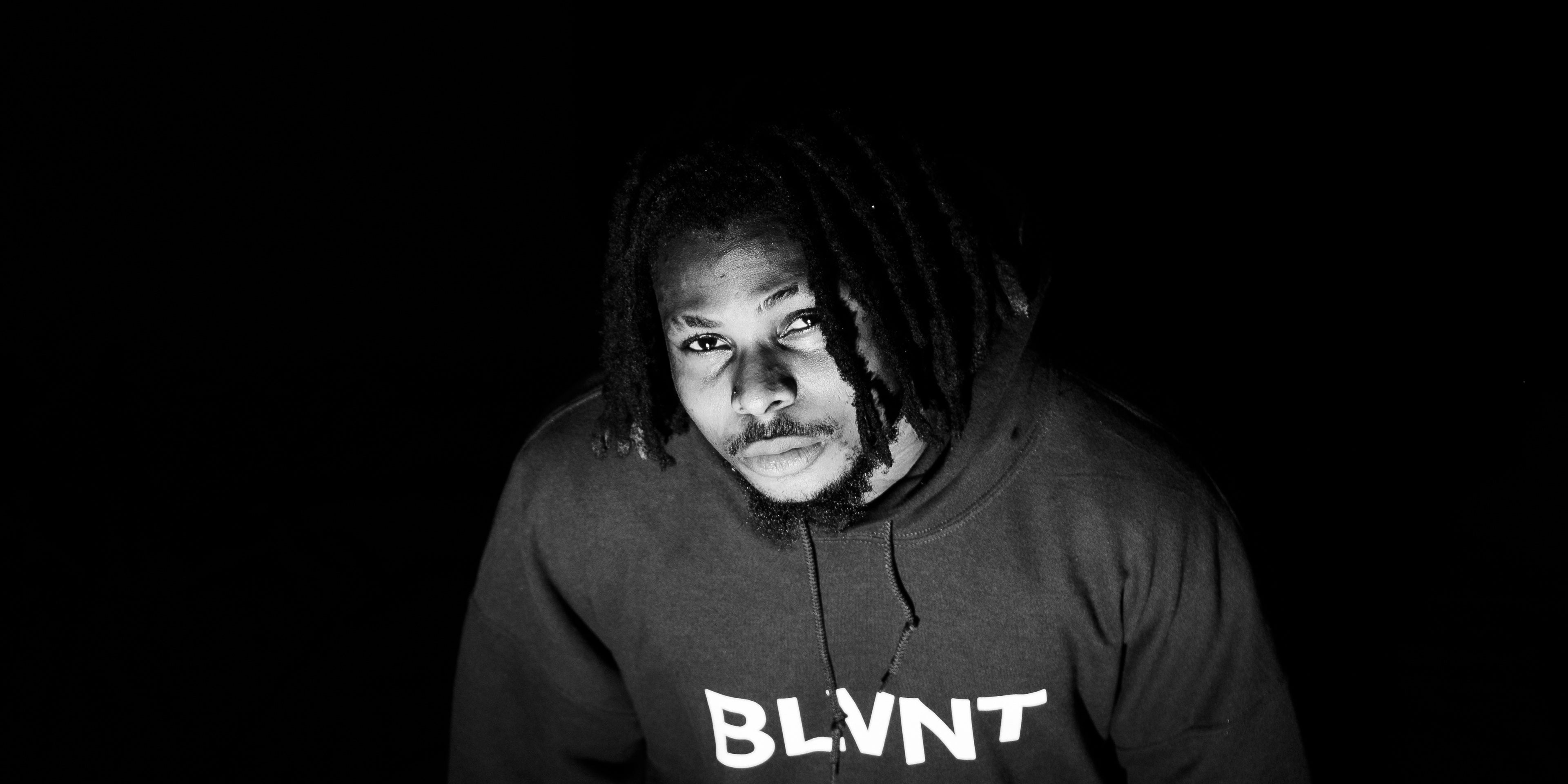 Figure in a BLVNT graphic hoodie photographed from above against a black ground