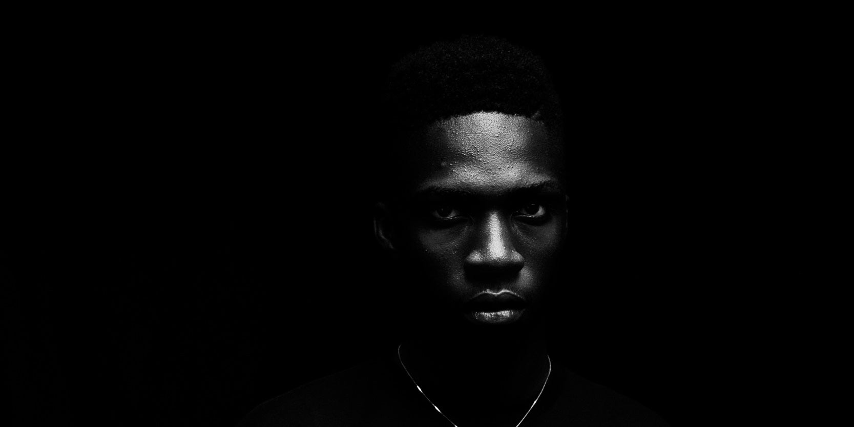 Close portrait in low light, a fine chain at the collar, against a black ground