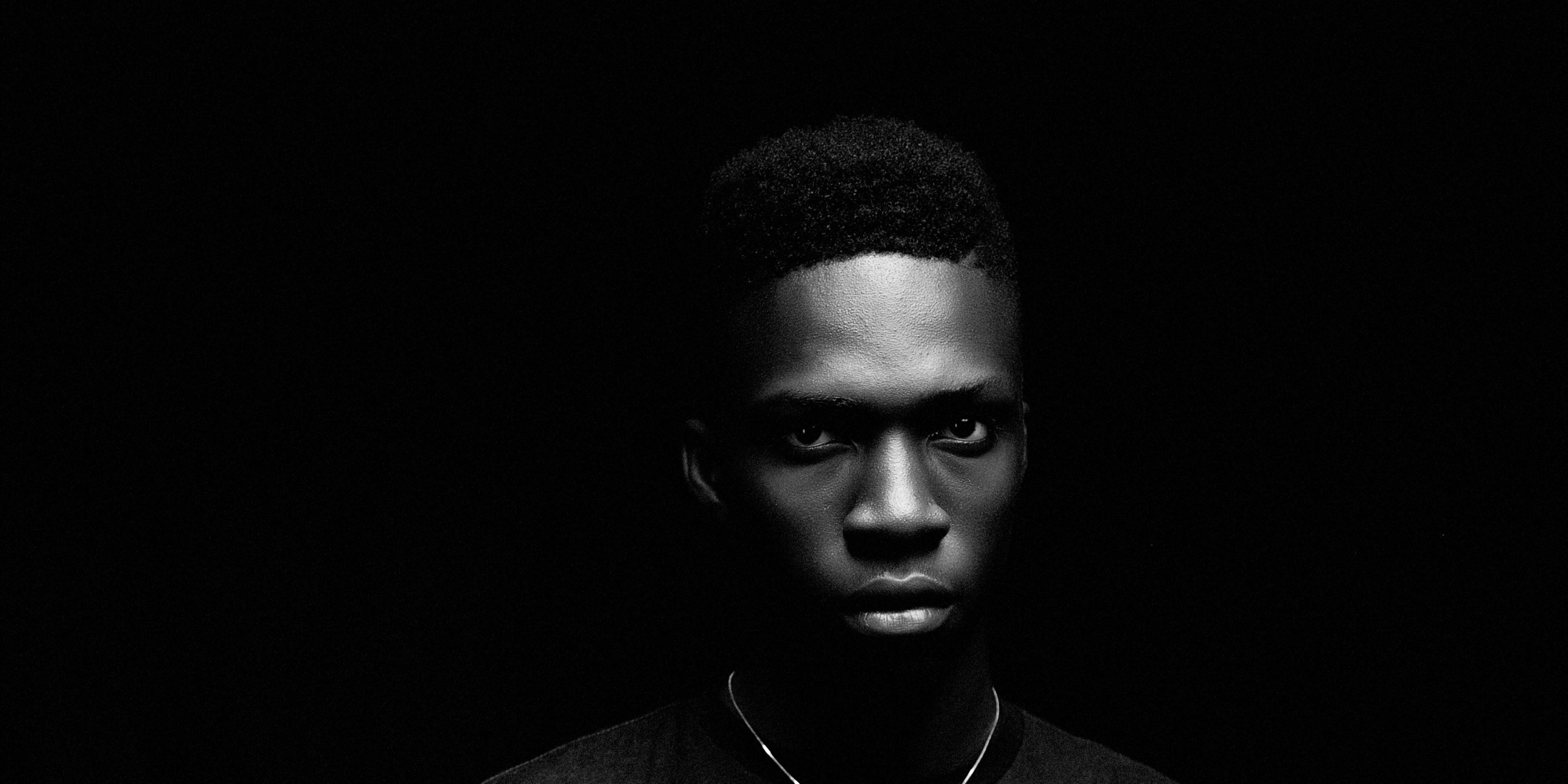 Close portrait in low light, a fine chain at the collar, against a black ground